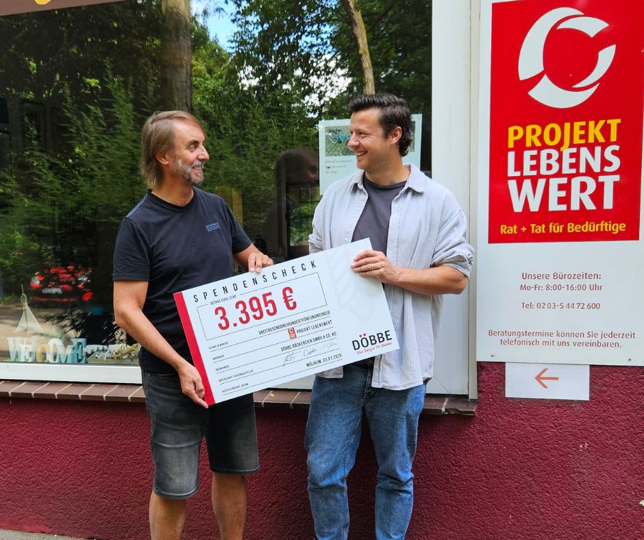 Zwei lächenlde Männer sehen sich an und halten einen Spendenscheck im Wert von 3.395€ in den Händen. Überreicht von der Bäckerei Döbbe. Im Hintergrund sieht man das Logo Projekt Lebenswert.