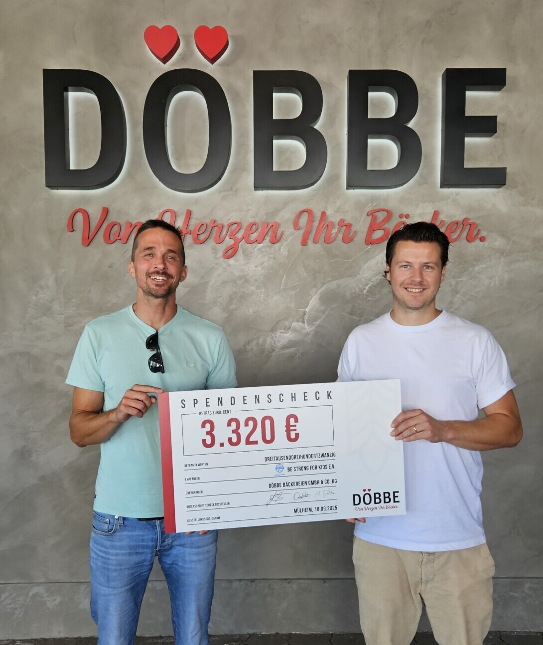 Zwei lächenlde Männer sehen sich an und halten einen Spendenscheck im Wert von 3.320€ in den Händen. Im Hintergrund sieht man das Logo Döbbe, von Herzen Ihr Bäcker.